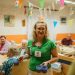 A caregiver serving drinks to elderly residents in a cheerful nursing home setting.