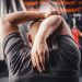 Man stretching arms in a gym, viewed from behind, focusing on fitness and flexibility.